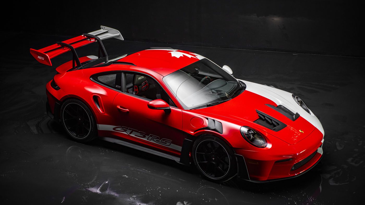 A red and white 911 GT3 RS with a large rear wing and a maple leaf design on the roof, photographed in a dark studio setting, reminiscent of models showcased at the Porsche Experience Center.
