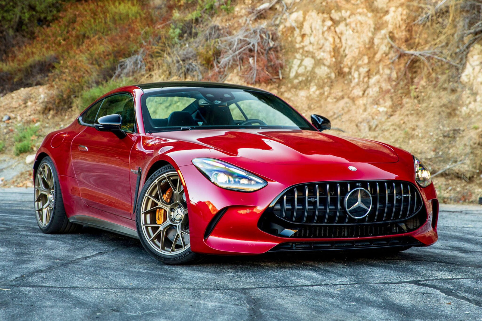 A red 2025 Mercedes-AMG GT63 S E Performance sports car is parked on a paved surface in front of a rocky hillside.