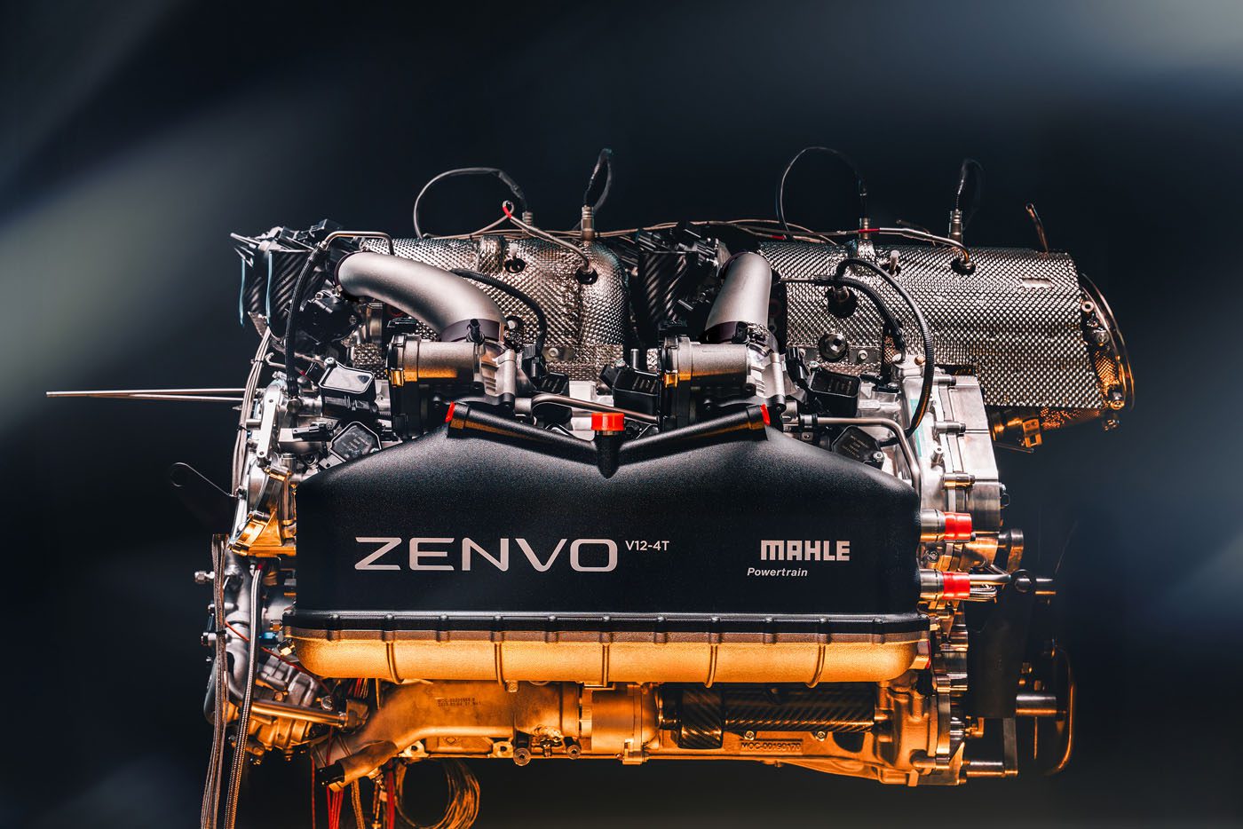 A high-performance Mahle Powertrain V12 engine, labeled "Zenvo V12-4T," with visible components shines against a gradient background, embodying the essence of a powerful road car.