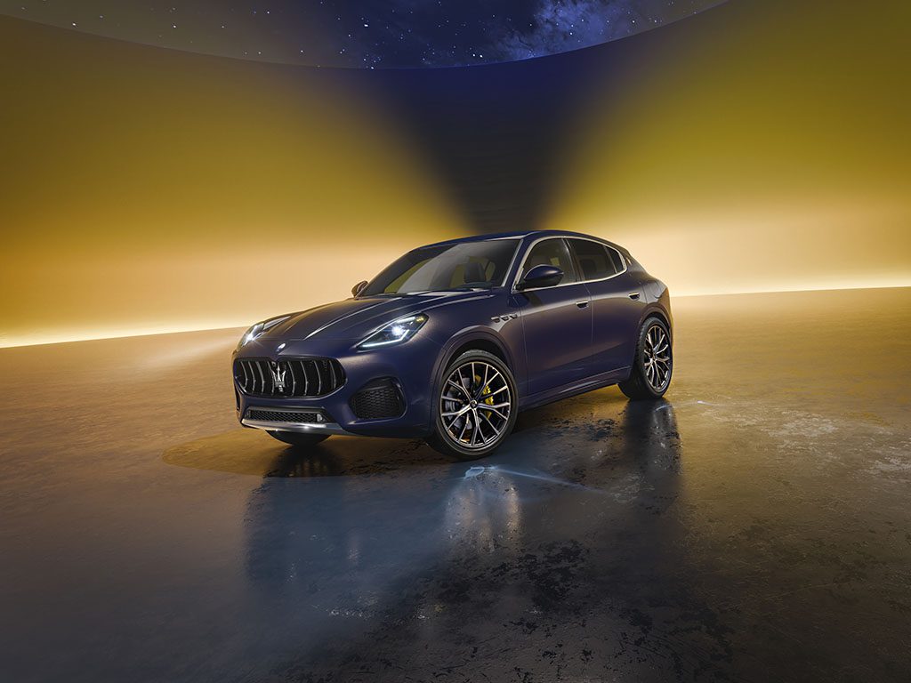 A dark blue Maserati SUV parked on a reflective surface with a gradient yellow and purple background.