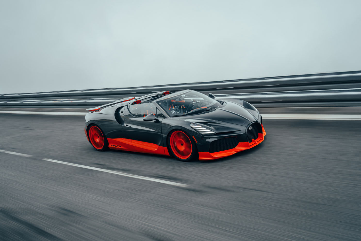 A sleek, black and red Bugatti W16 Mistral sports car speeds along a highway, with blurred motion emphasizing its world record-worthy fast movement.