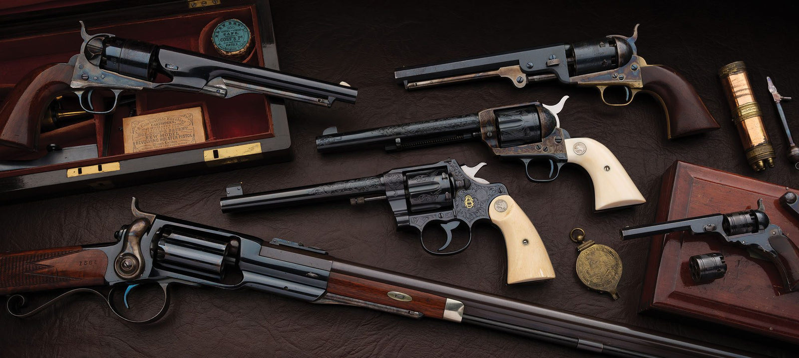 A collection of six vintage Colts with wooden and ivory grips, displayed on a dark surface with wooden cases and accessories, reminiscent of a firearm Concours d'Elegance.