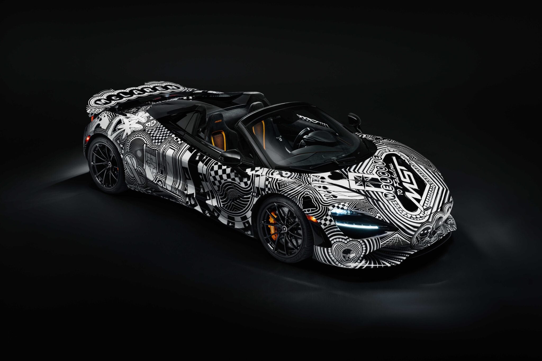A black sports car with white geometric and graphic patterns, inspired by Project Viva Revealed: One-of-One McLaren 750S Spider Brings Las Vegas to Life, is parked in a dark studio setting.