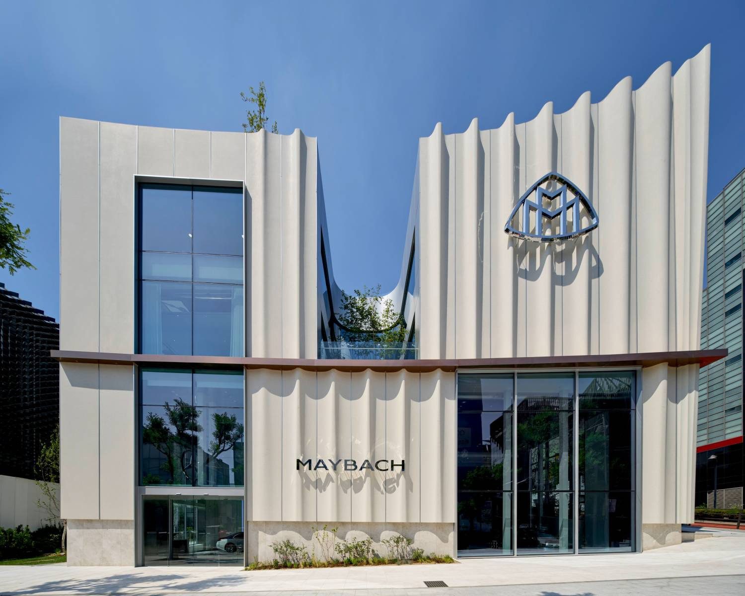 Modern Maybach showroom building with a wavy facade, large glass windows, the Maybach logo, and the brand name displayed above the entrance—home to the World's First Maybach Brand Center in Seoul.