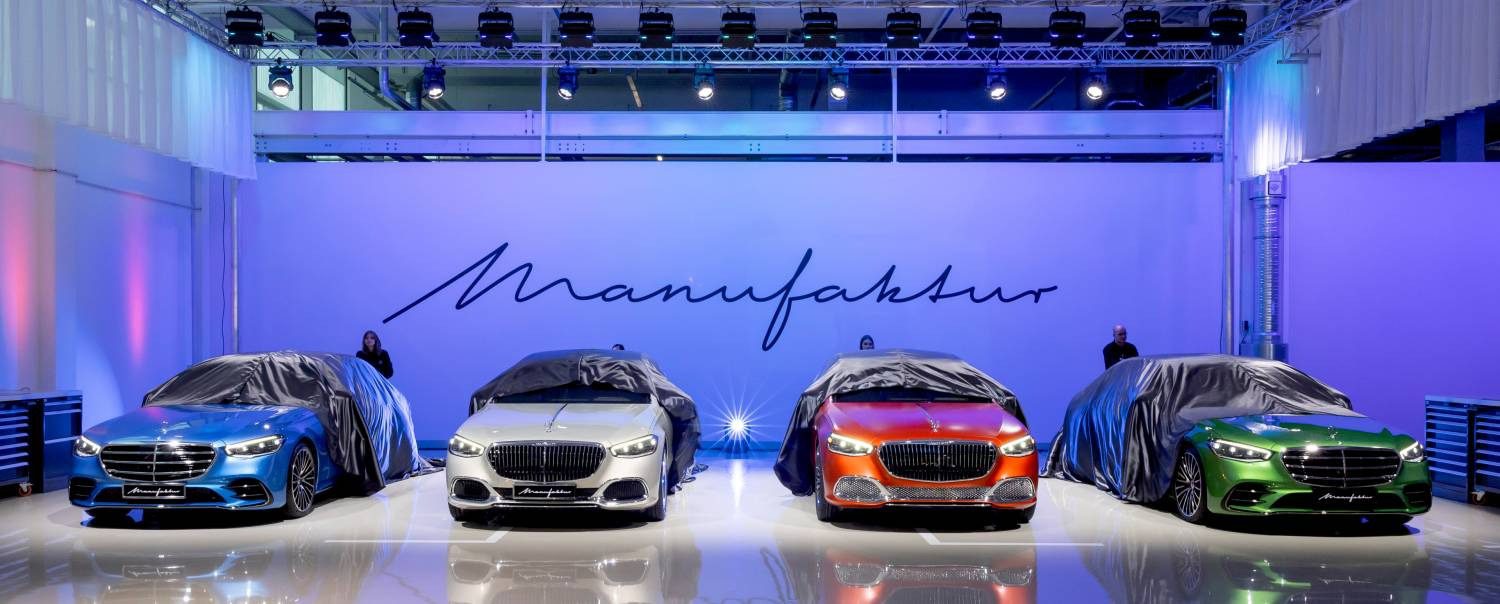 Four covered cars gleam under spotlights in the showroom, set against a "Manufaktur" sign. This MANUFAKTUR Studio highlights Mercedes-Benz's dedication to customization, showcasing tailored craftsmanship for the discerning driver.