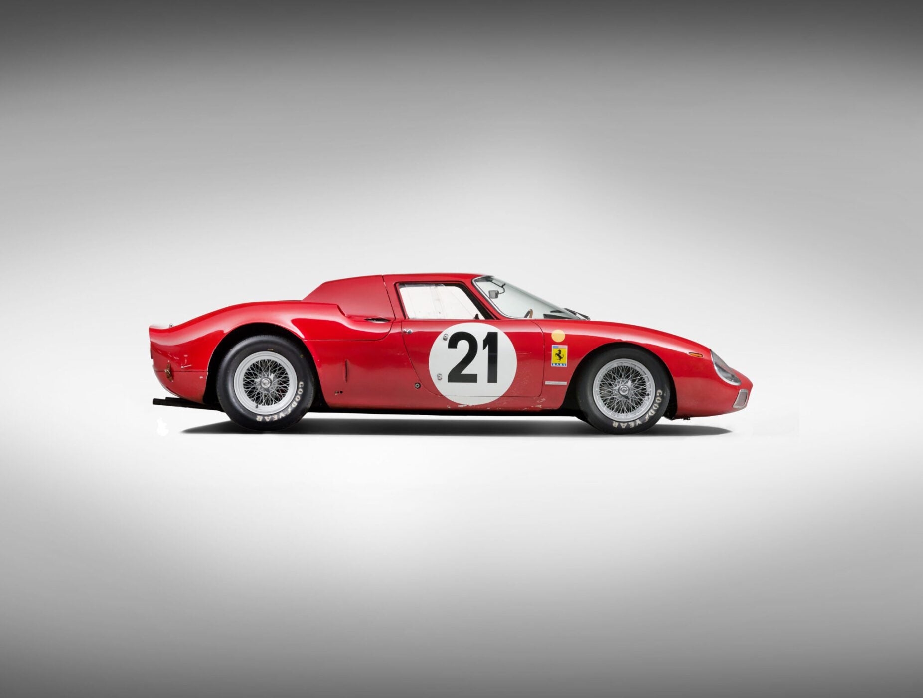 Side view of a red vintage sports car, reminiscent of a Ferrari 250 LM with the number 21 on the side, boasting a sleek, aerodynamic design that echoes its Le Mans-winning legacy against a neutral background.