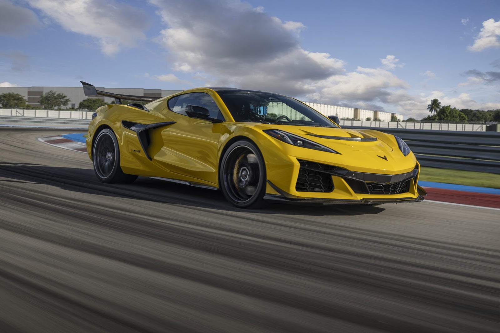 A yellow sports car speeding on a race track with motion blur and a cloudy sky in the background.