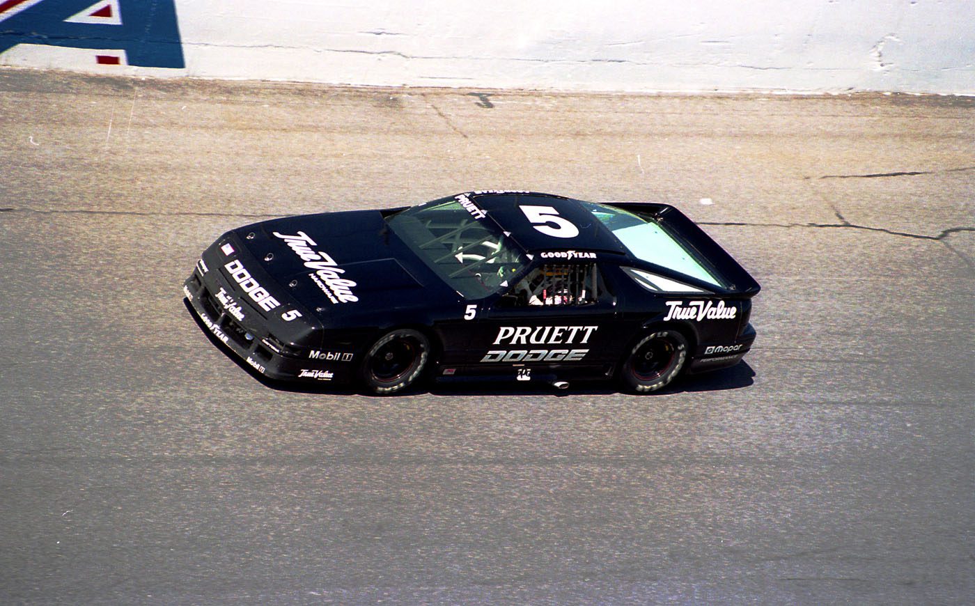 A black race car with the number 5 and "Pruett Dodge" branding speeds around Laguna Seca during the 2025 Rolex Monterey Motorsports Reunion, celebrating IROC All-Star Legends on the iconic racetrack.
