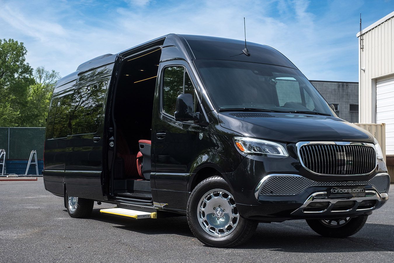 A black Sprinter Serenus Plus luxury van with an open sliding door and visible red interior seats is parked outdoors on a sunny day.