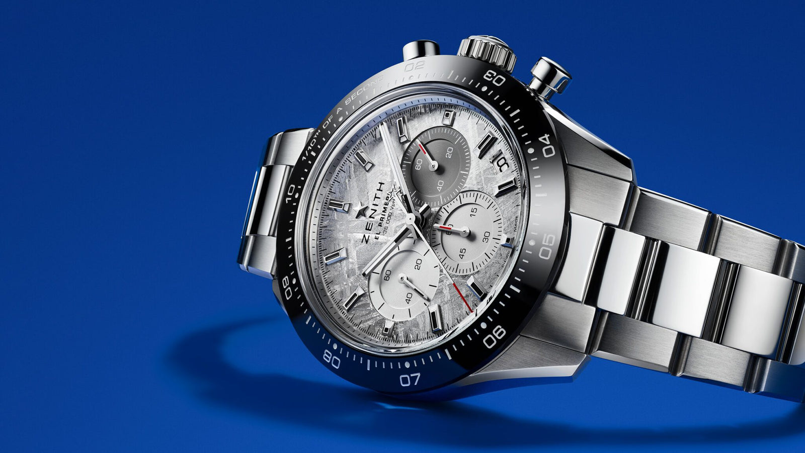 A stainless steel Cosmic Chronograph wristwatch with a textured silver dial and three subdials, positioned on a blue background.