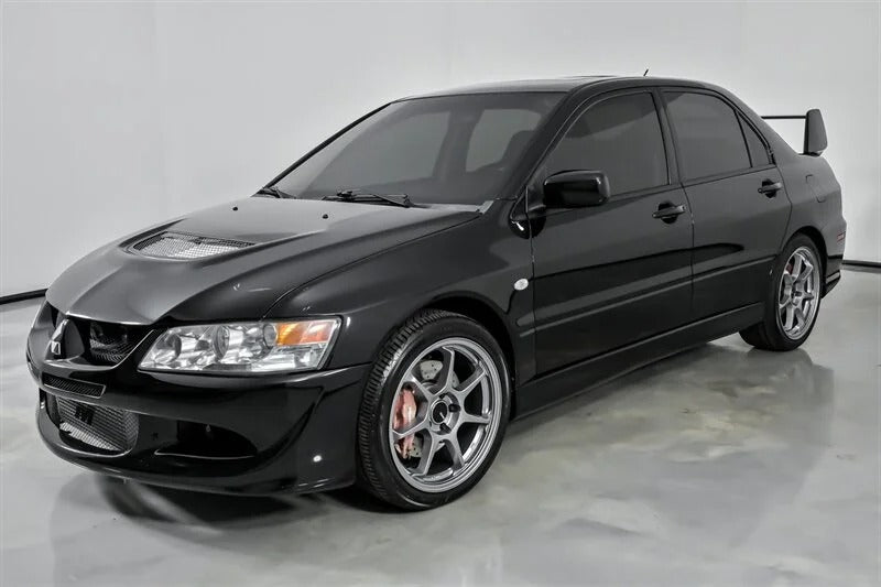 A black Mitsubishi Lancer Evolution sedan with tinted windows, alloy wheels, a hood vent, and a rear spoiler—one of the best manual transmission cars for sale—parked in a plain indoor setting.