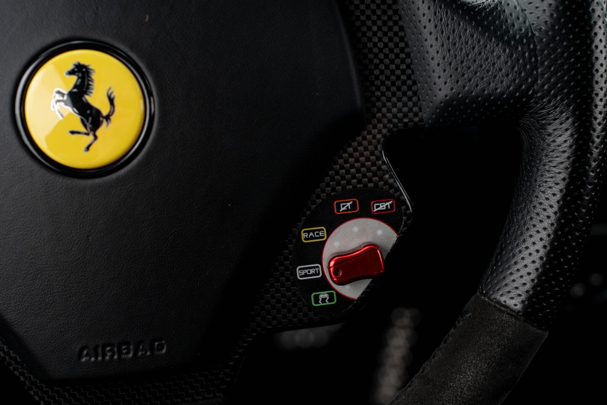 Close-up of a Ferrari steering wheel showing the logo, airbag label, and drive mode selector—offering a glimpse of Your Chance To Own The Final Ferrari That Michael Schumacher Helped Develop.