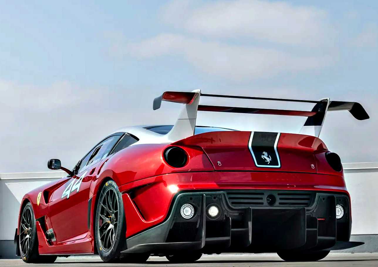 A striking Ferrari 599XX EVO with black accents and a large rear wing is parked outdoors under a partly cloudy sky, awaiting its debut at the Monterey auction.