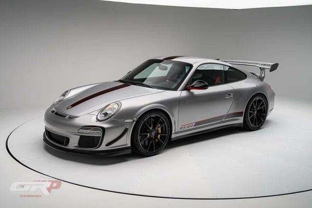 An ultra-rare silver PTS 911 GT3 RS 4.0 sports car with black and red racing stripes, black wheels, and a large rear wing, displayed in a well-lit studio setting by Graham Rahal Performance.