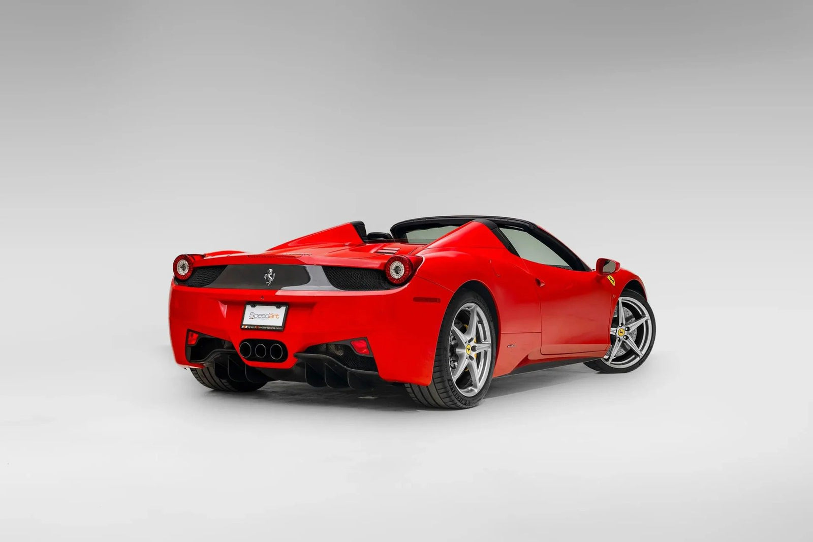 A red Ferrari 458 convertible sports car is shown from the rear three-quarter view against a plain, light gray background—an iconic example for those seeking the best Ferrari among cars for sale.