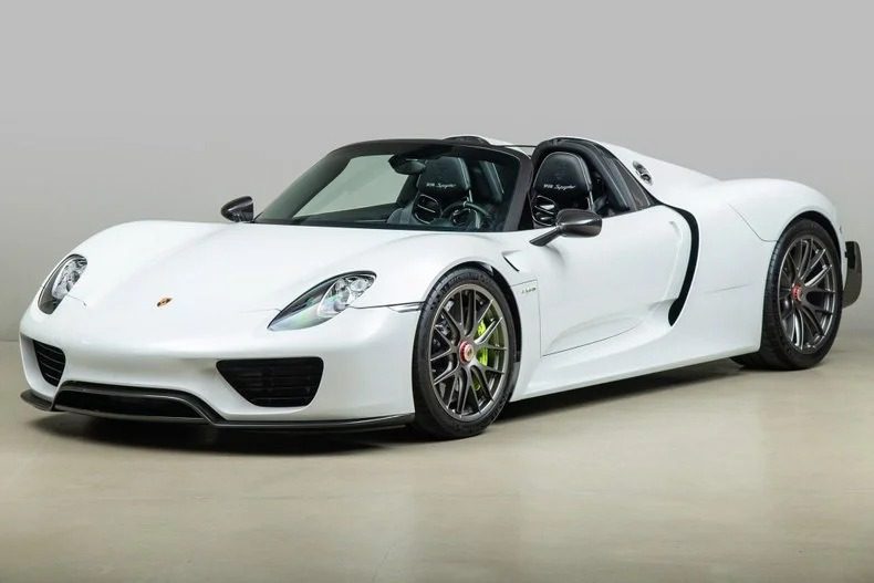A white Porsche 918 Spyder with a sleek design, two doors, and black accents, parked on a smooth surface.