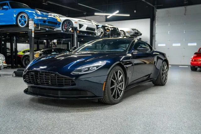 A sleek black Budget Brawn sports car is parked in a showroom, showcasing elegant curves among other cars on lifts in the background.
