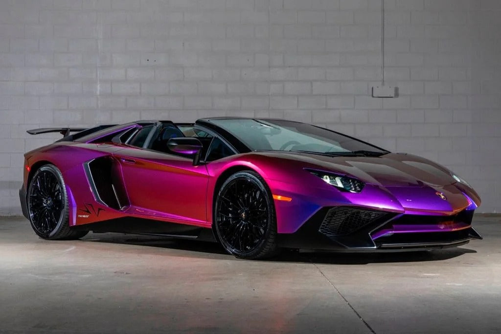 A purple Lamborghini Aventador convertible with black wheels, featuring a powerful V12 engine, parked indoors against a white brick wall—perfect for exotic cars enthusiasts.