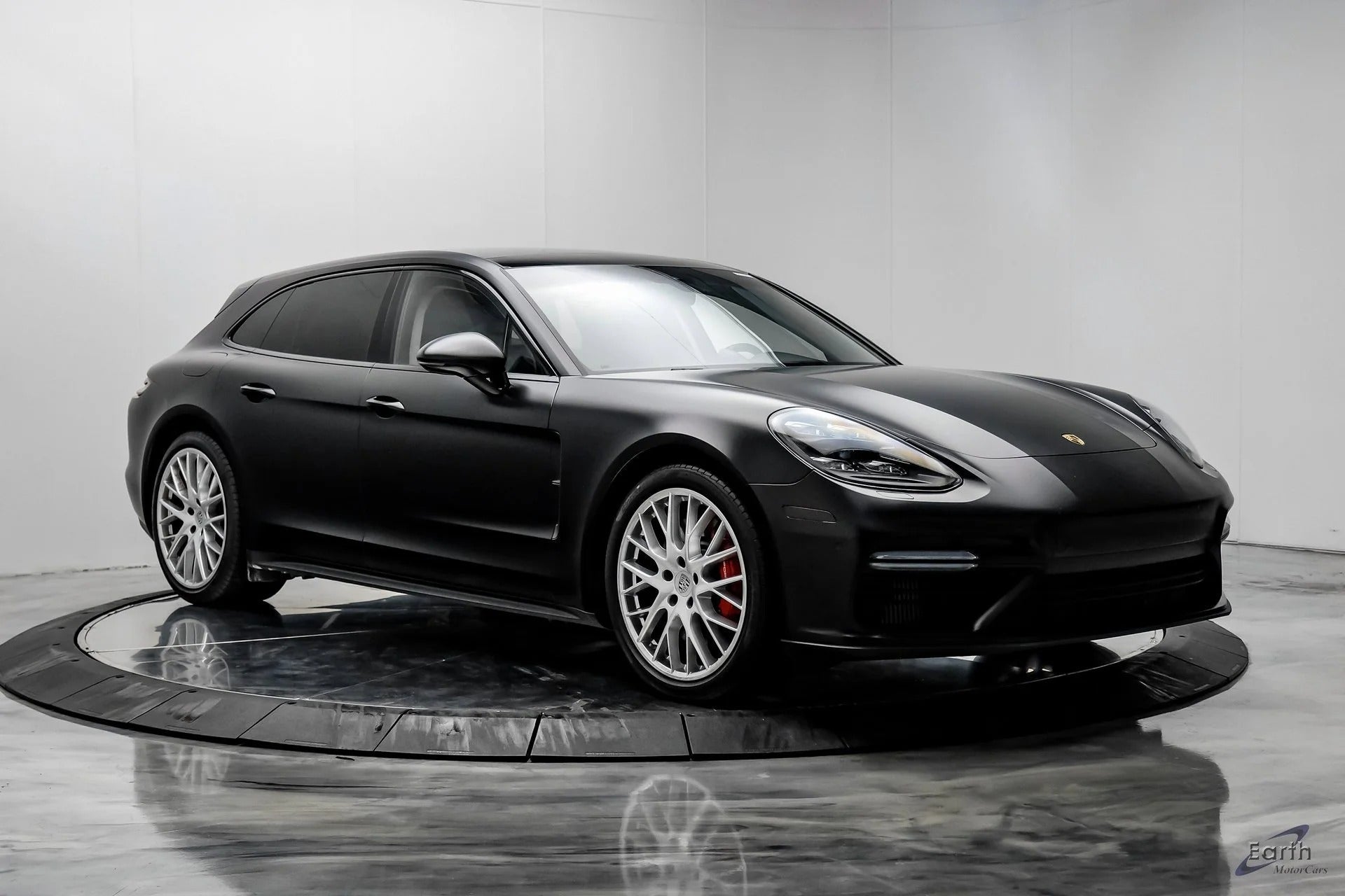 A black Porsche Panamera Sport Turismo wagon, part of the Luxury Performance Wagons category, is displayed in a modern showroom with a white background and reflective floor.