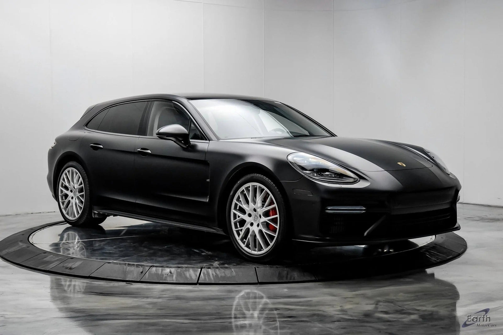 A black Porsche Panamera Sport Turismo wagon, part of the Luxury Performance Wagons category, is displayed in a modern showroom with a white background and reflective floor.