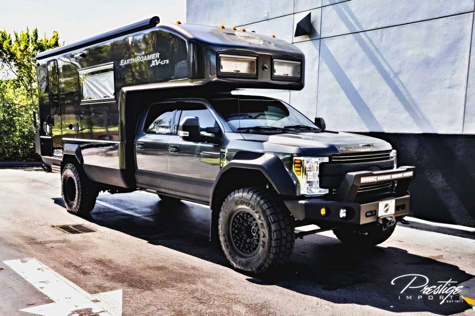 A large, black EarthRoamer XV-LTS expedition vehicle—your chance to Live Off the Grid in Luxury—is parked on a sunlit street next to a building, its rugged tires and off-road features on full display. 2019 EarthRoamer XV-LT listed for sale.