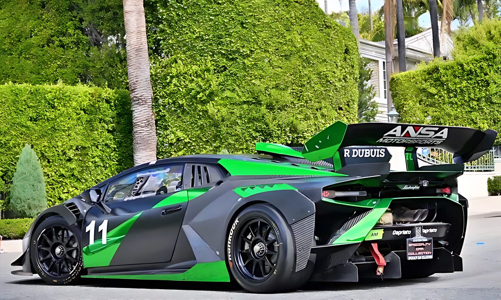 A green and black race car with number 11 and a large rear wing is parked on a street in front of manicured bushes and palm trees—an eye-catching contender among the best supercars under $200k.