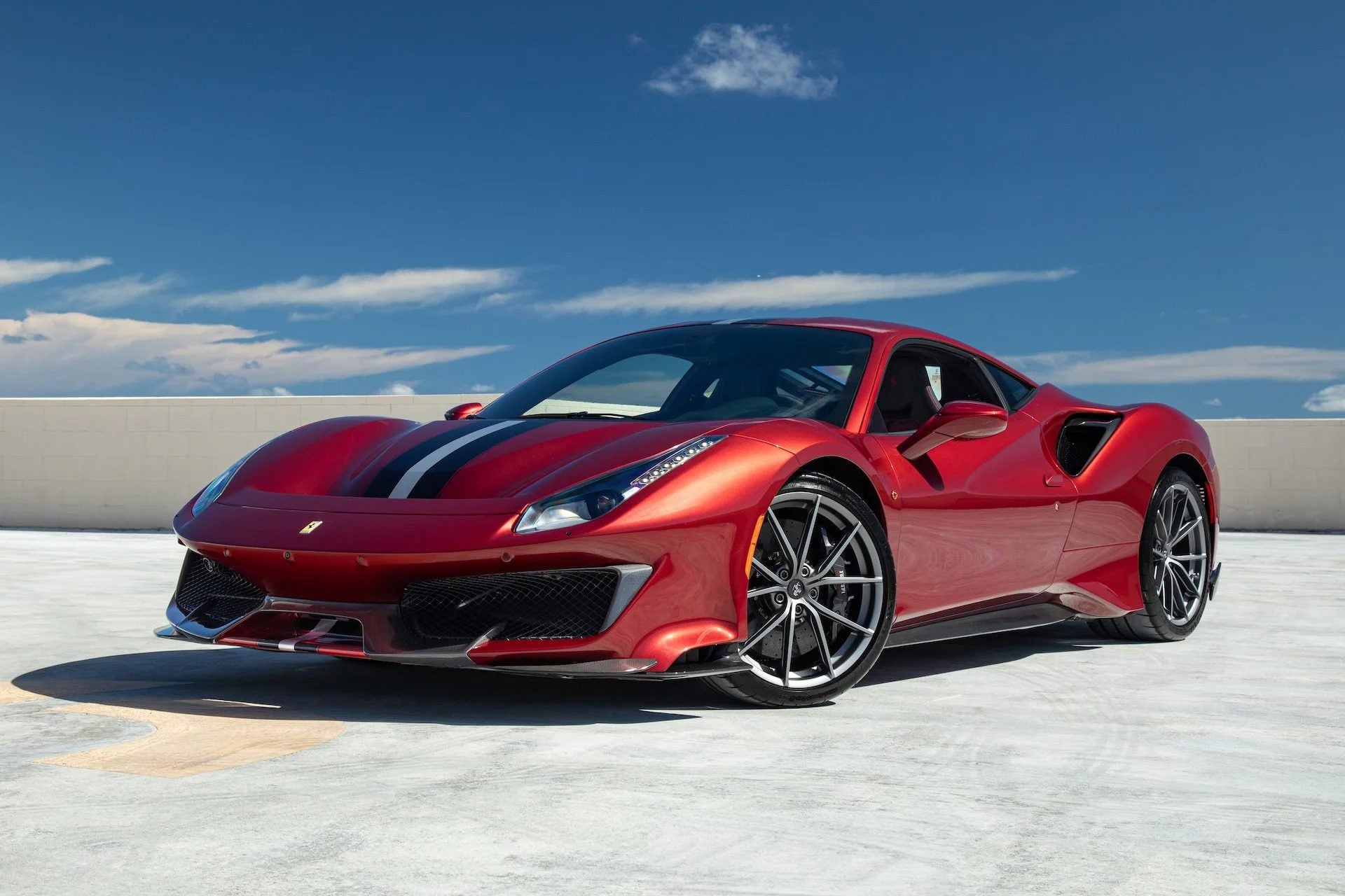 A track-ready Ferrari 488 Pista with black racing stripes is parked on a rooftop under a clear blue sky.