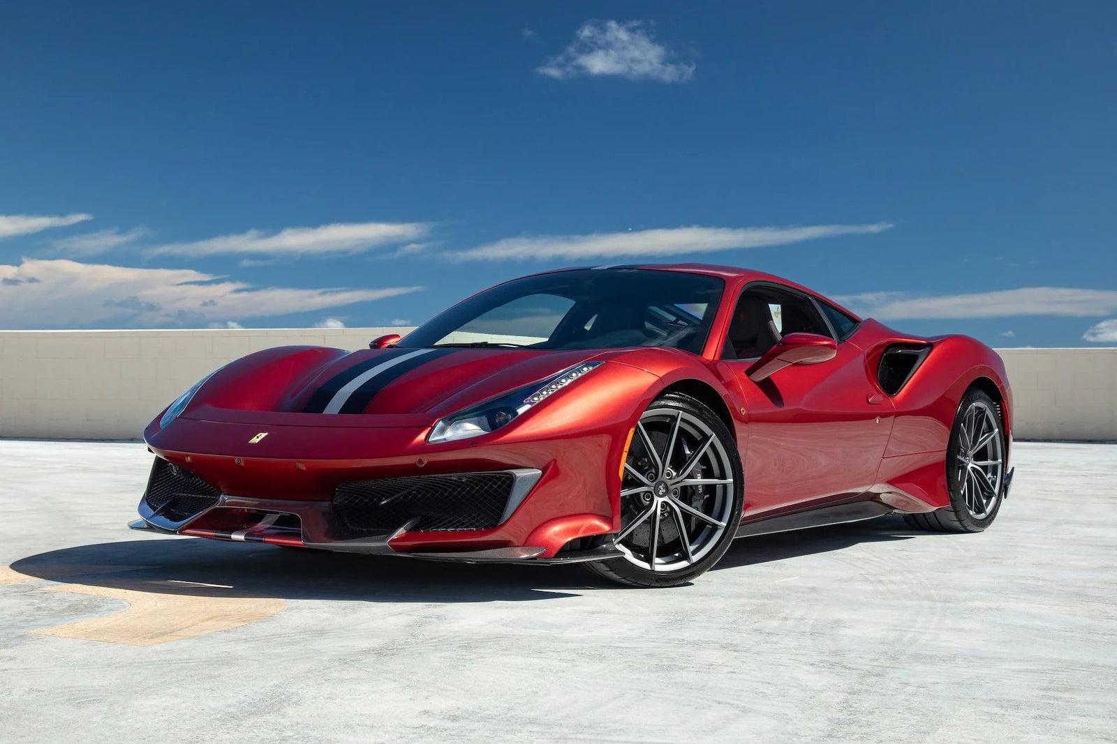 A track-ready Ferrari 488 Pista with black racing stripes is parked on a rooftop under a clear blue sky.