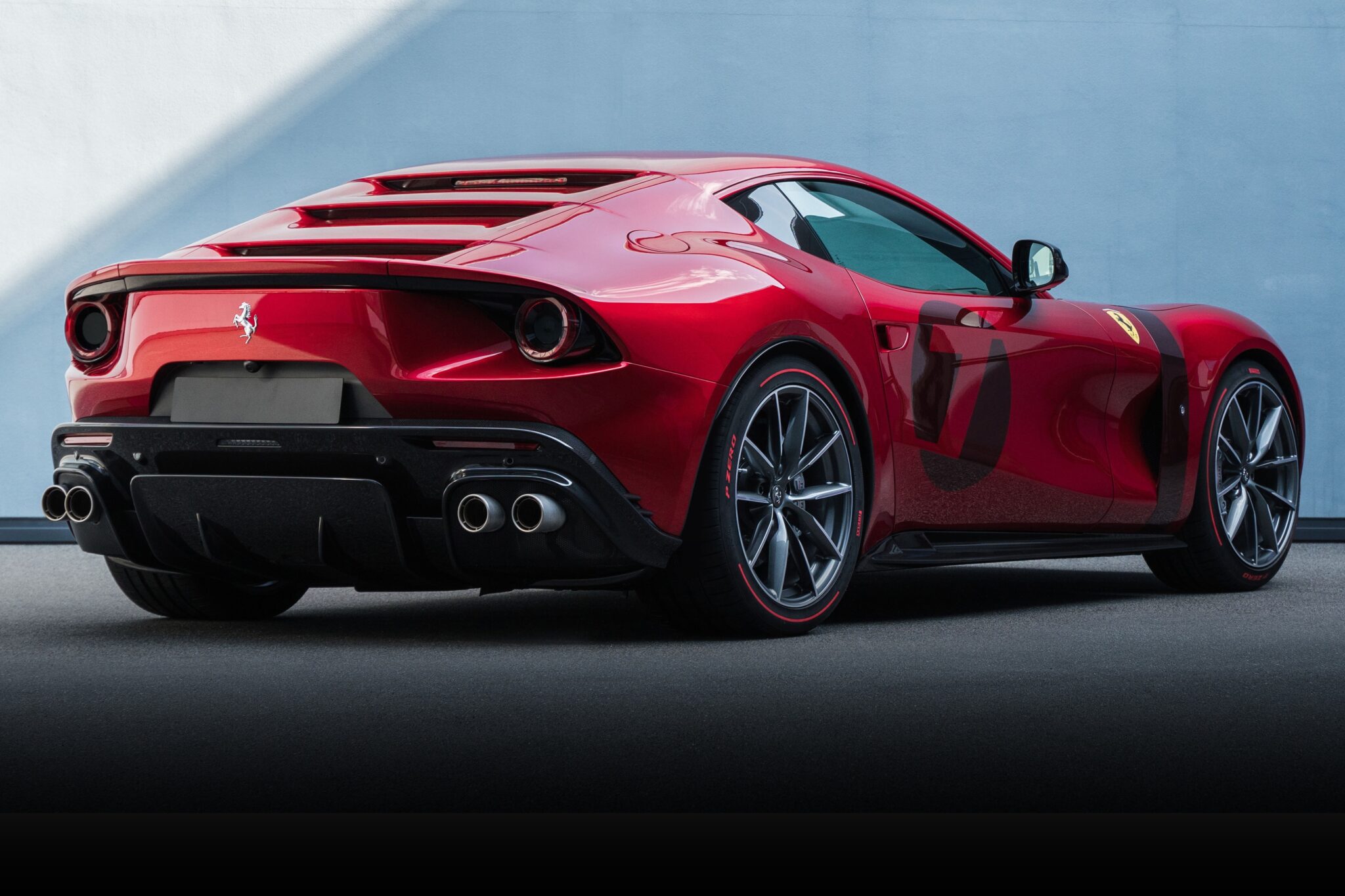 A red Ferrari sports car, one of the 1-of-1: Rarest Ferraris In The World, is parked on a smooth surface, shown from the rear side angle against a plain light blue wall.