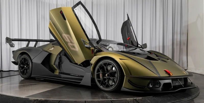 A green Lamborghini Essenza SCV12 with open scissor doors is showcased in a showroom setting, highlighting its sleek race car design, black wheels, and aerodynamic details.