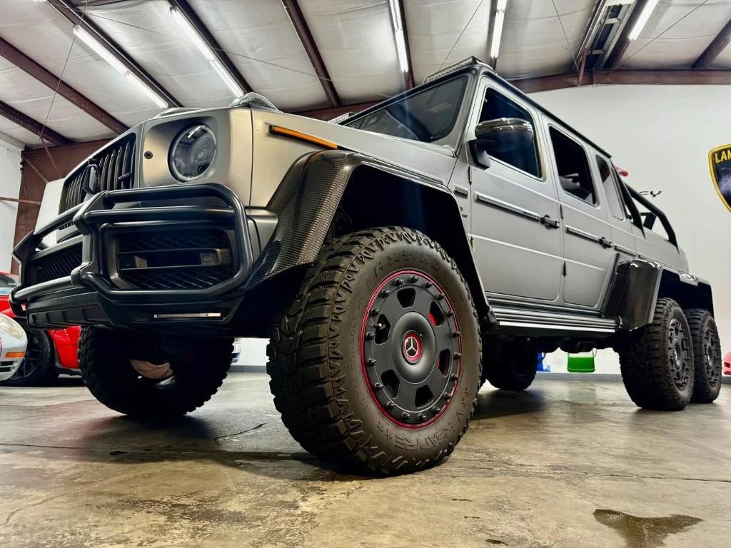 A matte gray Mercedes-Benz G 63 AMG 6x6 pickup truck is parked indoors on a concrete floor under a metal roof, showcasing the bold appeal of 6x6 trucks for sale.
