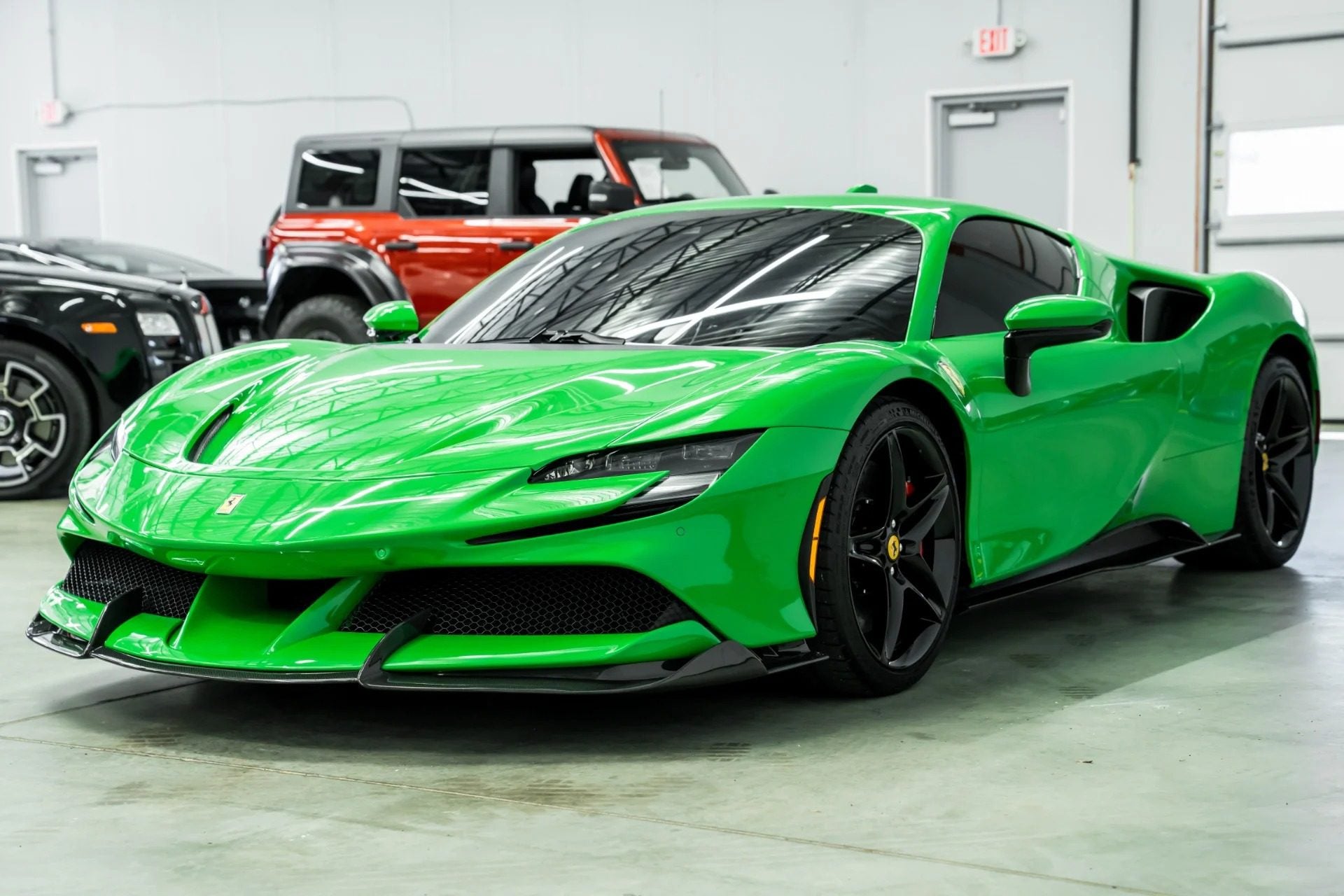 A bright green Ferrari with black wheels is parked indoors on a concrete floor near other vehicles, showcasing one of the bold Ferrari colors.