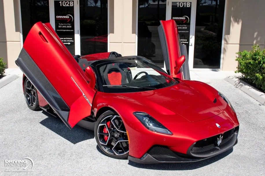 A red sports car with butterfly doors open, parked on a driveway in front of storefronts, exudes the opulence of luxury cars. It's as if Santa's Super Sleighs took a modern twist this Christmas season.