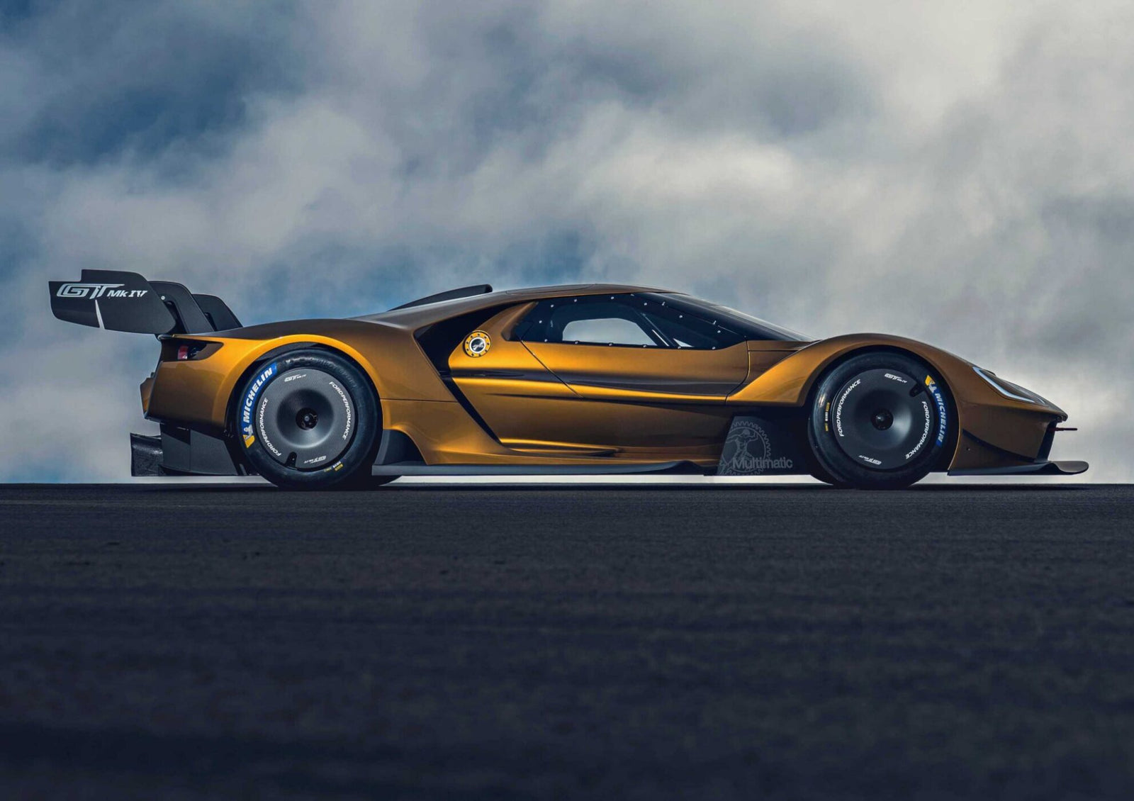 A gold Ford GT Mk IV—part of the Ford Performance Launches Final Production Run of Legendary Ford GT Mk IV—is shown from the side on a dark road, featuring a large rear wing and aerodynamic design, with cloudy skies in the background.