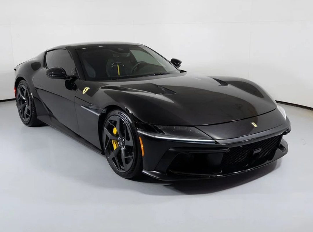 A black Ferrari 12Cilindri sports car with yellow brake calipers is displayed in a well-lit showroom with a white background, highlighting this exceptional 2025 Ferrari for sale.