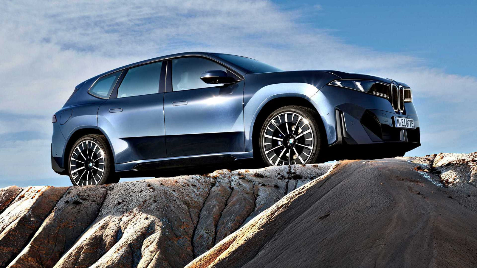 A blue BMW SUV, embodying the BMW iX3 Launches the Neue Klasse Era With 400-Mile Range and 463 HP, is parked on rocky terrain under a clear sky, viewed from a side angle.