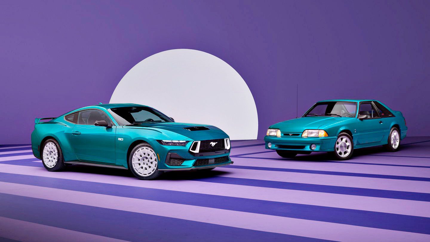 Two teal Ford Mustang cars, including a classic and a Fox-Body Mustang GT, are parked indoors on a striped purple floor with a large white semicircle backdrop.