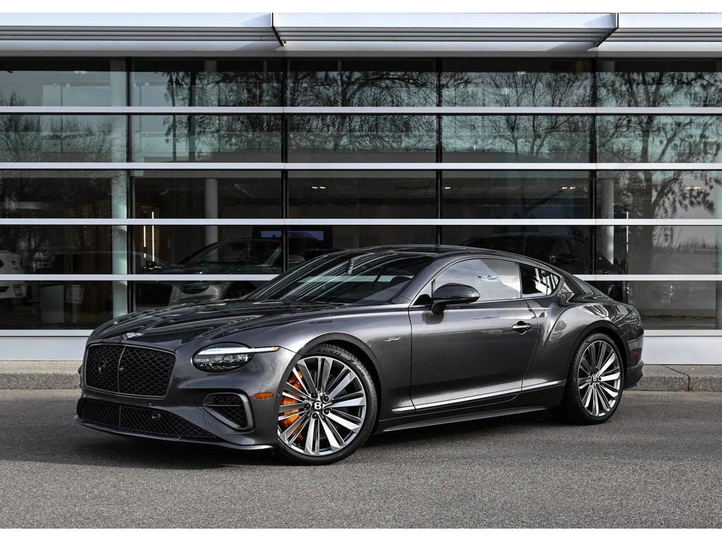 A dark gray luxury coupe, one of the best Bentleys with large alloy wheels, is parked in front of a modern glass building.