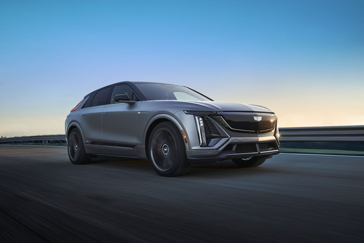 A gleaming 2026 Cadillac Lyriq-V glides along the road at sunset, its sleek design catching the last rays of daylight against a clear sky backdrop.
