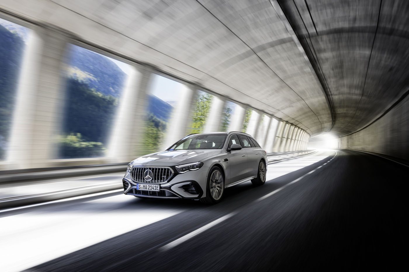 A sleek silver Mercedes-AMG E 53 HYBRID glides effortlessly through a curved tunnel, with light streaming in from the side openings.
