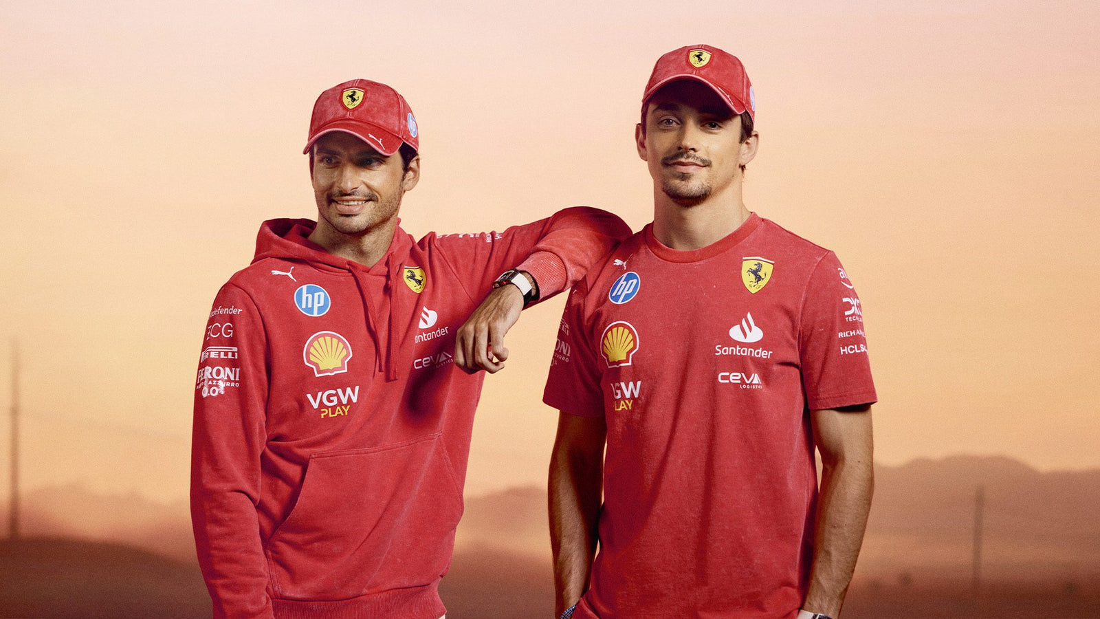 Two individuals in red Scuderia Ferrari team uniforms and caps stand against a sunset background, embodying the spirit of the Desert Sun Collection.