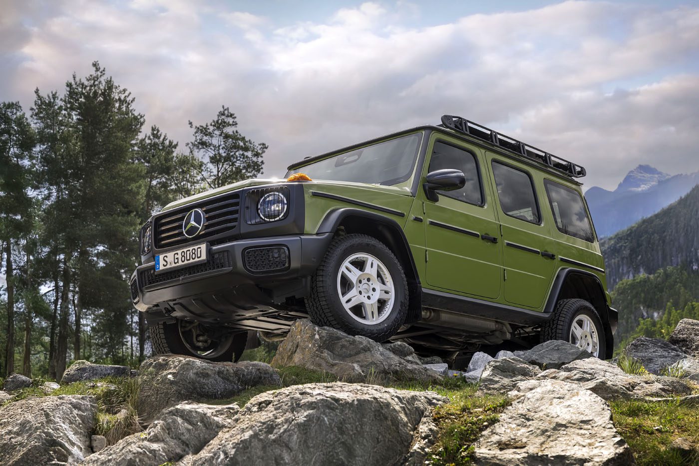 A green Mercedes-Benz G-Class 1-of-460 SUV is parked on rocky terrain outdoors, with trees and mountains in the background under a partly cloudy sky—STRONGER THAN THE 1980s.