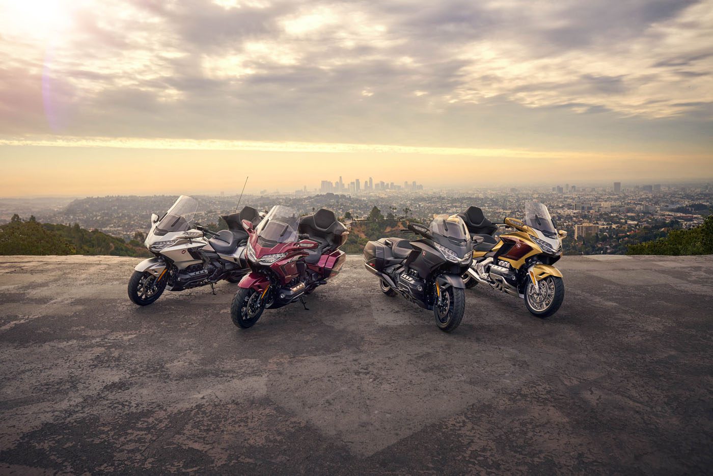 Four Special Edition Honda Gold Wing motorcycles are parked on a hill, majestically overlooking the city skyline beneath a cloudy sky.