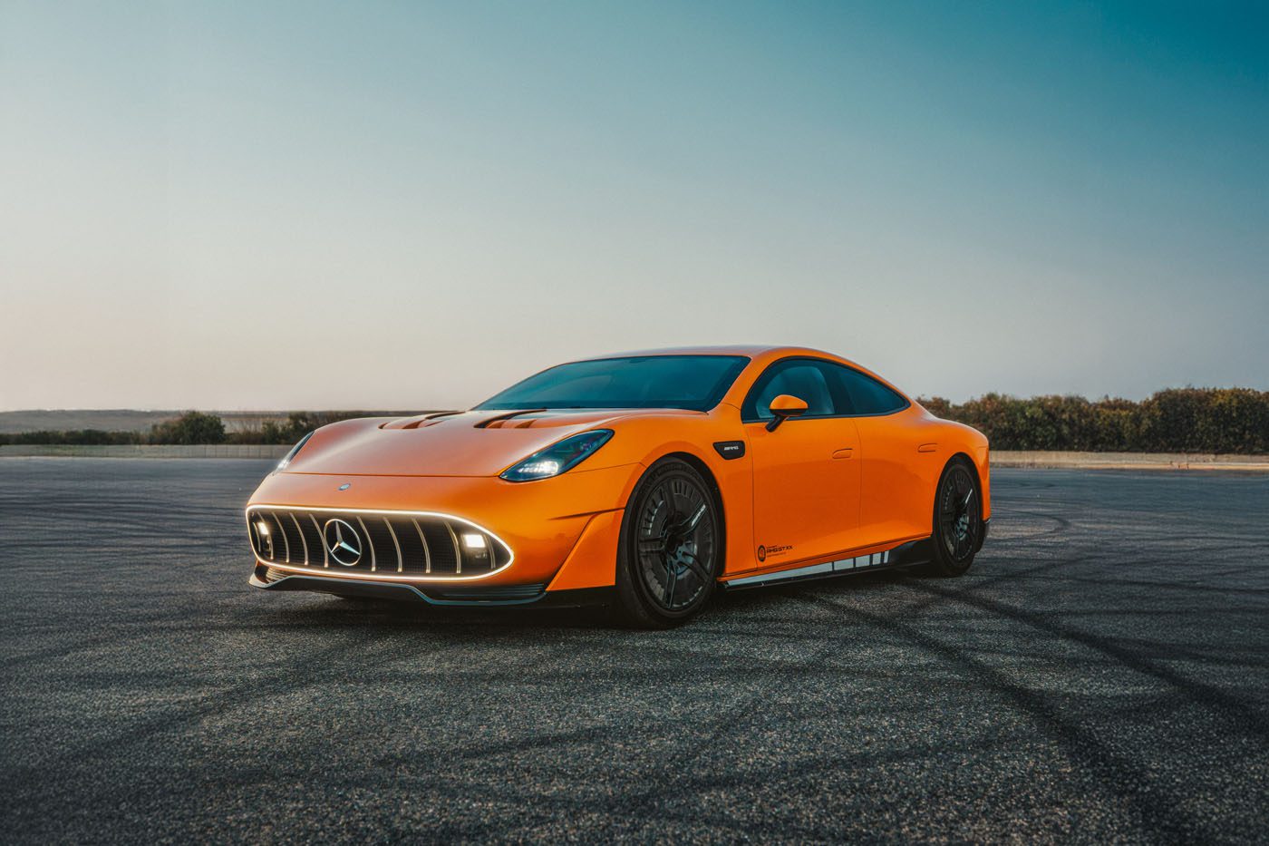 An orange CONCEPT AMG GT XX Mercedes-Benz sports car is parked on an empty, sunlit asphalt surface with clear skies, ready for an exhilarating drive around the world.