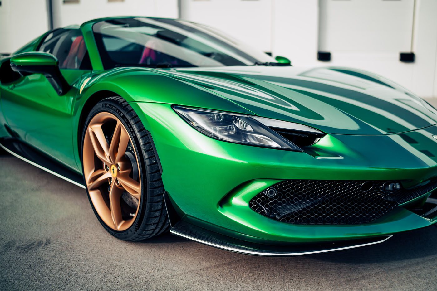 A close-up view of a shiny green Ferrari 296 GTS with gold wheels, a modern tribute parked on a concrete surface.