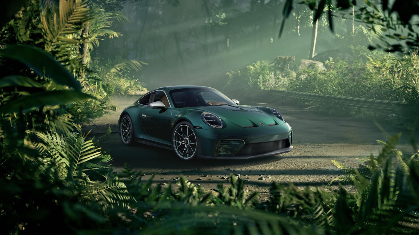 A stunning green Porsche Sonderwunsch 911 GT3 is parked on a dirt road, surrounded by dense, lush jungle vegetation with sunlight filtering through the trees.