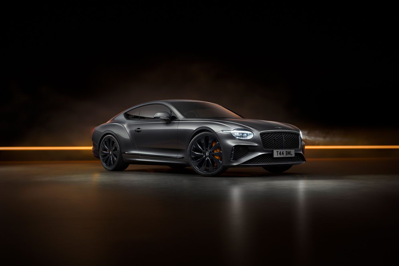 A sleek, dark grey Bentley sports car, part of the exclusive Black Edition series, with black rims and glowing headlights is showcased against a dark background accentuated by a horizontal orange light strip.