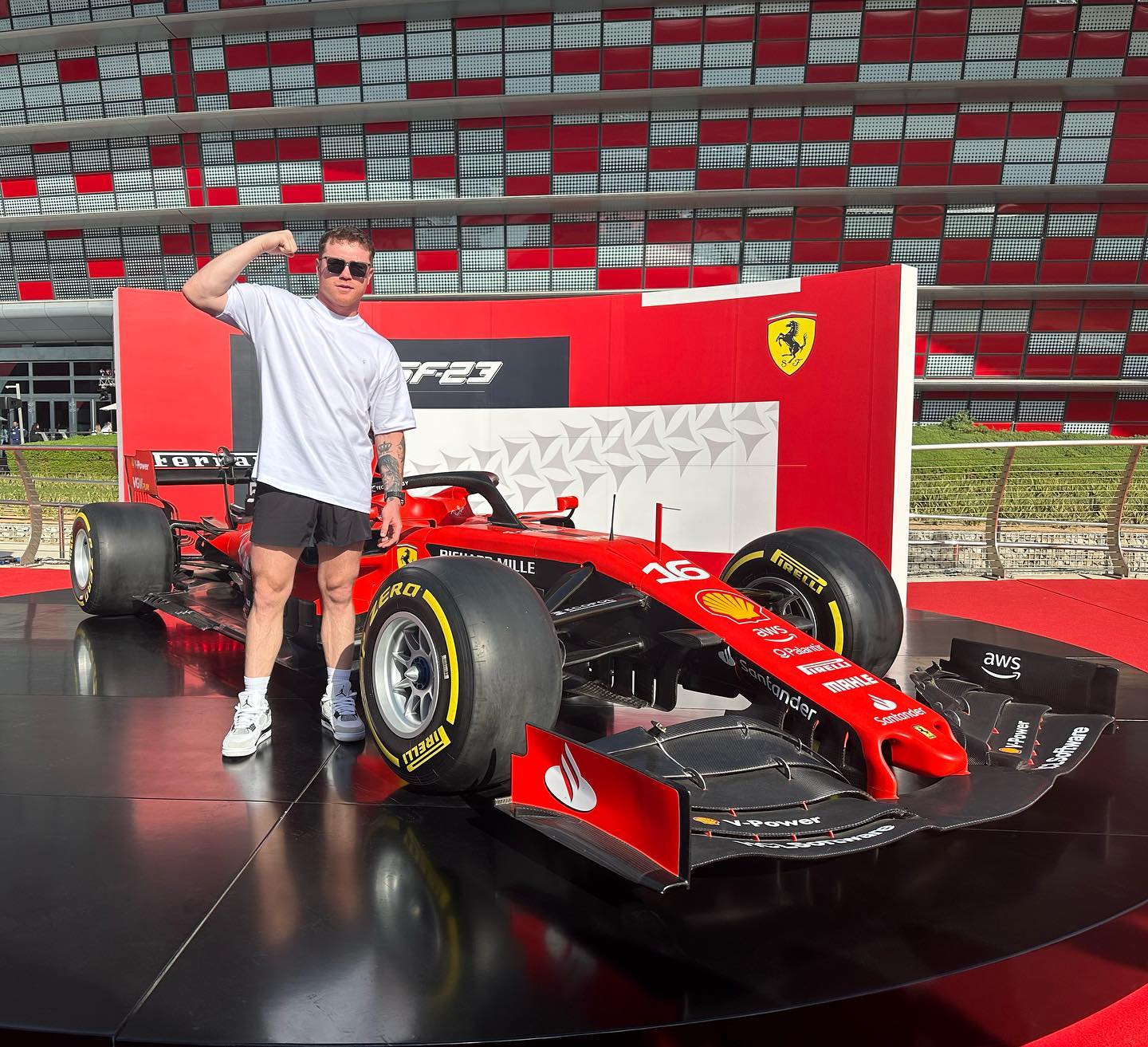 Person posing next to a red Ferrari supercar with iconic branding, in front of a striking red and white building that echoes the prestige of hypercars.