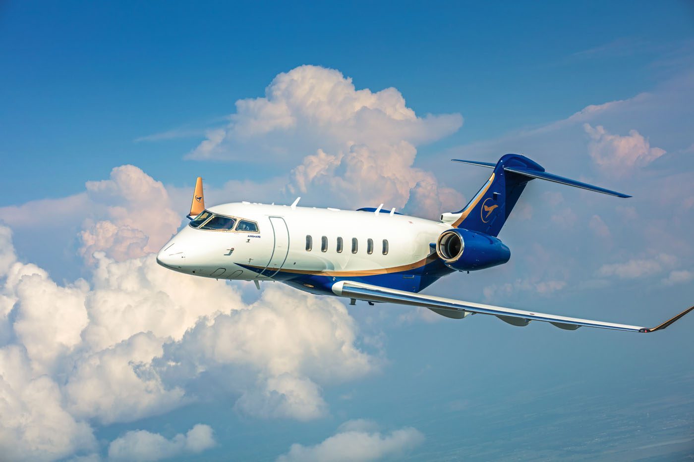 Small jet airplane flying through the sky with clouds in the background.
