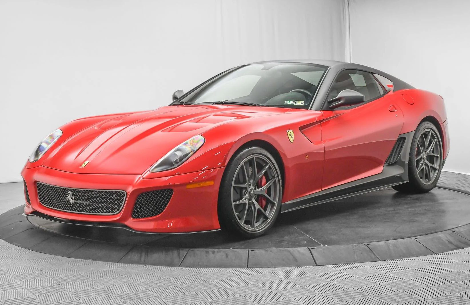 A red Ferrari 599 GTO with black alloy wheels is on display in a well-lit showroom with a gray background—a must-have addition for any supercar collection.